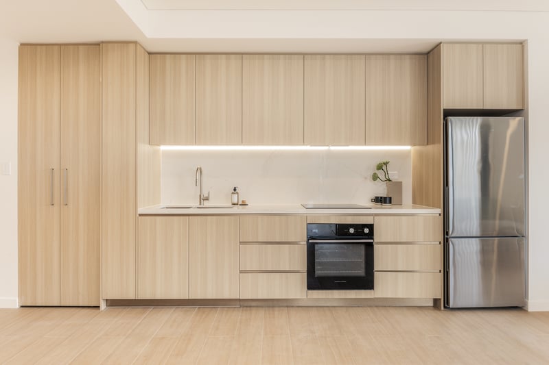 One bedroom kitchen at Arte Living Caringbah with timber joinery, stone splashback, oven and fridge