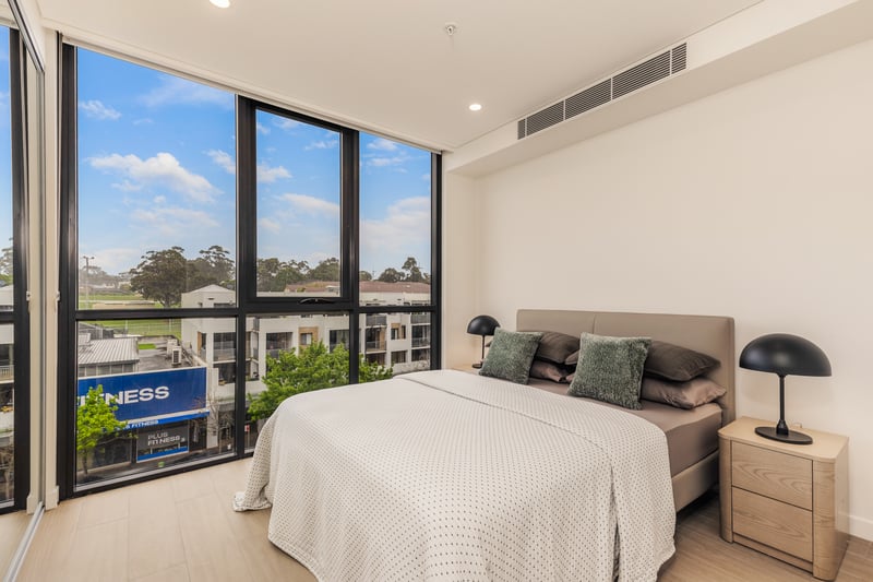 Separate bedroom with queen bed and corner floor-to-ceiling windows in an Arte Living Caringbah one bedroom apartment