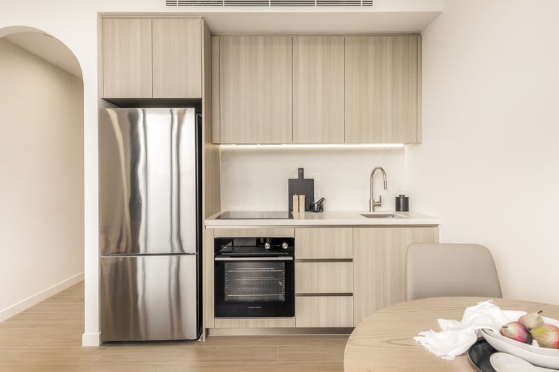 Studio kitchen at Arte Living Caringbah with timber joinery, stone benchtop, oven and fridge